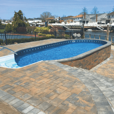 Radiant semi in-ground pool with paver decking and black fencing in a Michigan backyard